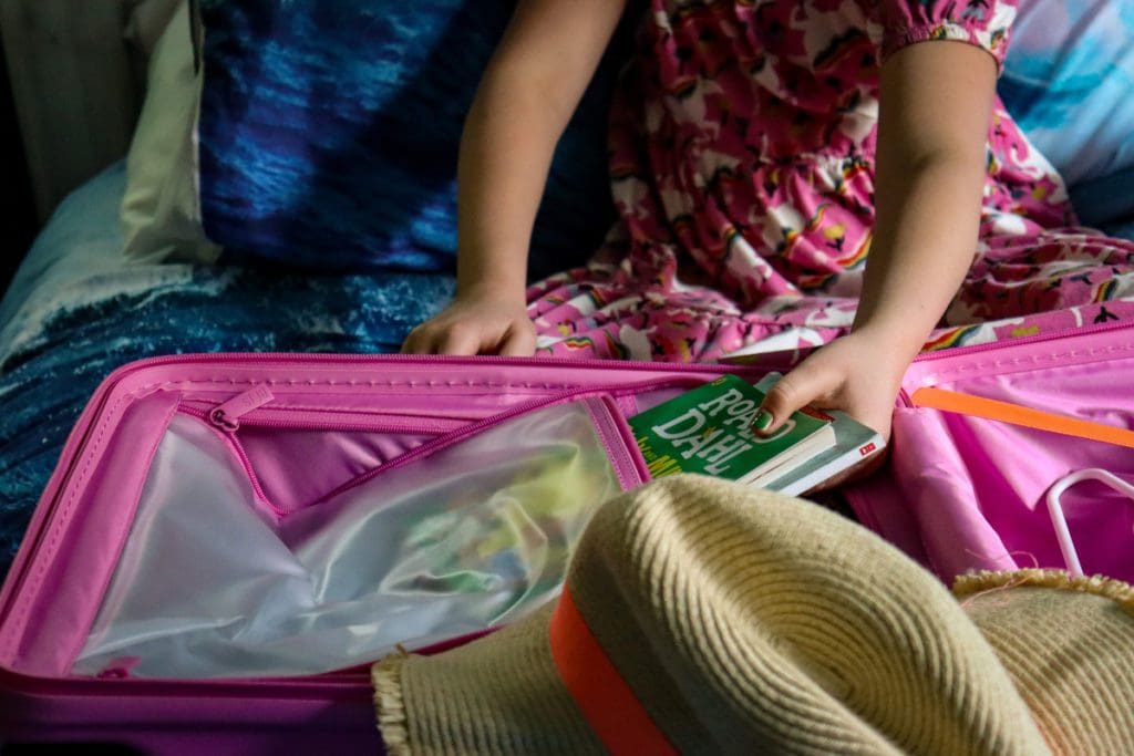 A young girl places a book in an interior pocket within the BÉIS Kids Roller.