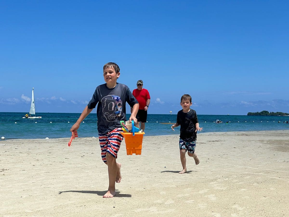 Two young kids run along the sand of a beach, while staying at Beaches Negril.