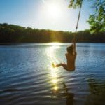 A young boy swings from a rope swing into a New York lake.