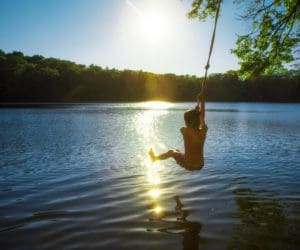 A young boy swings from a rope swing into a New York lake.