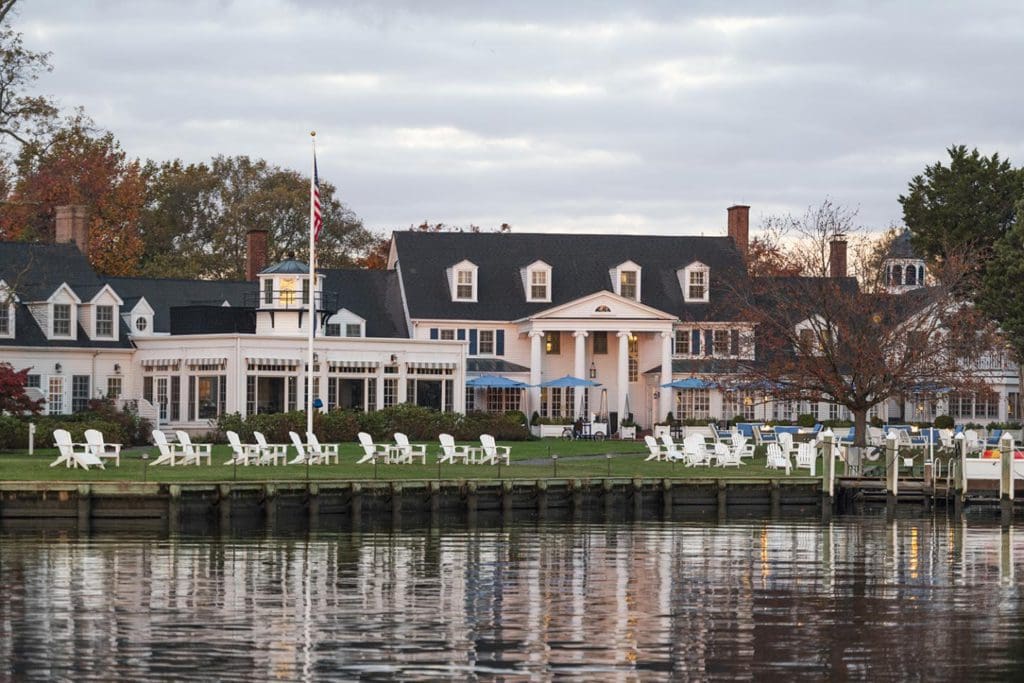 The exterior of Inn at Perry Cabin along the water, with several Adirondack chairs stationed on the waterfront.