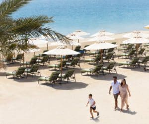A family of three walks across a beach in Dubai, while staying at Raffles The Palm Dubai.