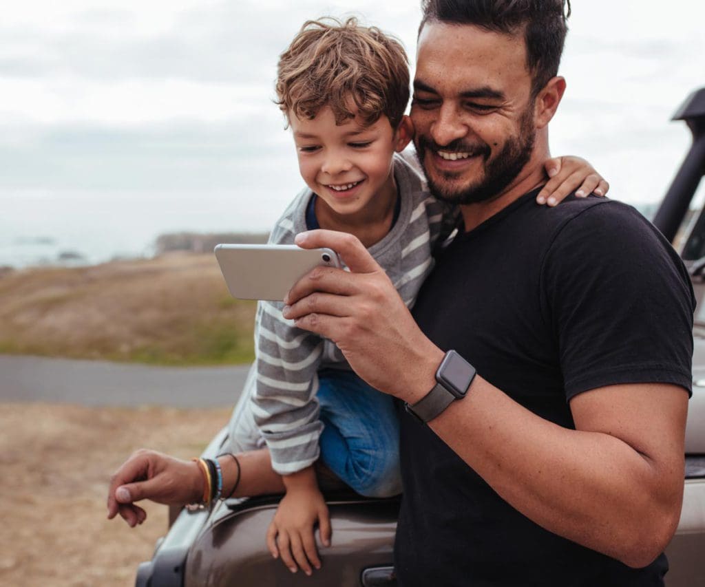 A dad and his young son watch a travel video on a smart phone.