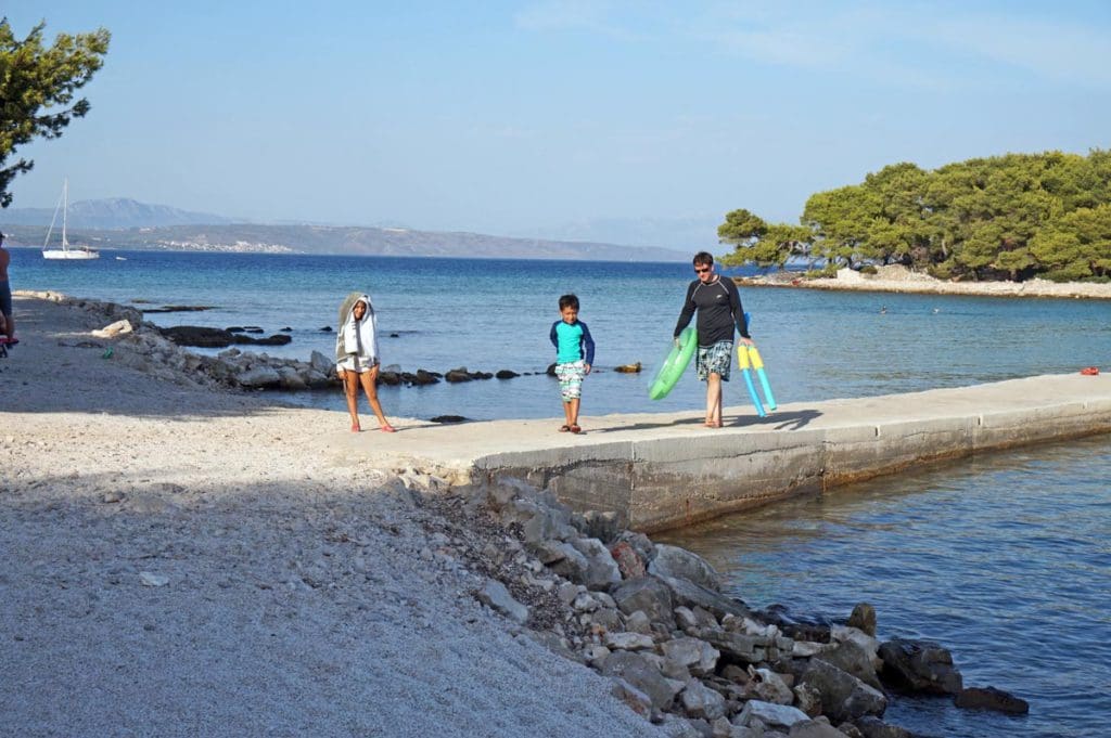 Two kids and their dad walk near the waters of Croatia with ocean toys.