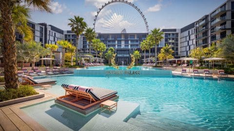 A pool chair faces the pool at Caesars Palace Dubai, with a Farris wheel in the distance.