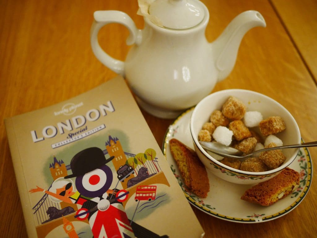 A London travel guide sitting on a table next to a pot of tea and cup of sugar.
