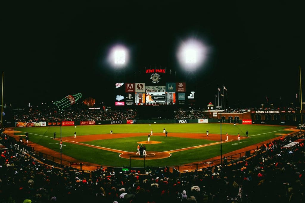 A baseball field with its flood lights on at night.