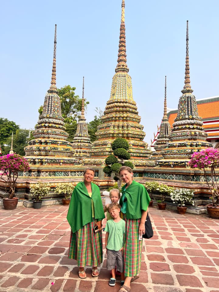 A mom and her two kids stand with another woman in front of a temple in Thailand, one of the best places to visit in Asia with kids.