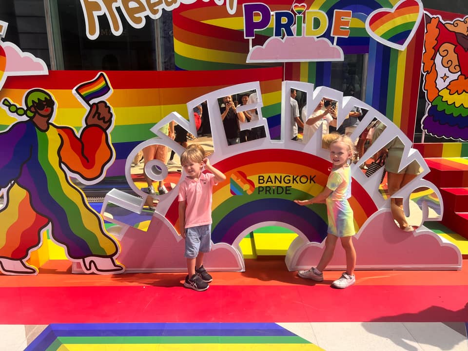 Two kids standing in front of a Thai "pride" parade float.
