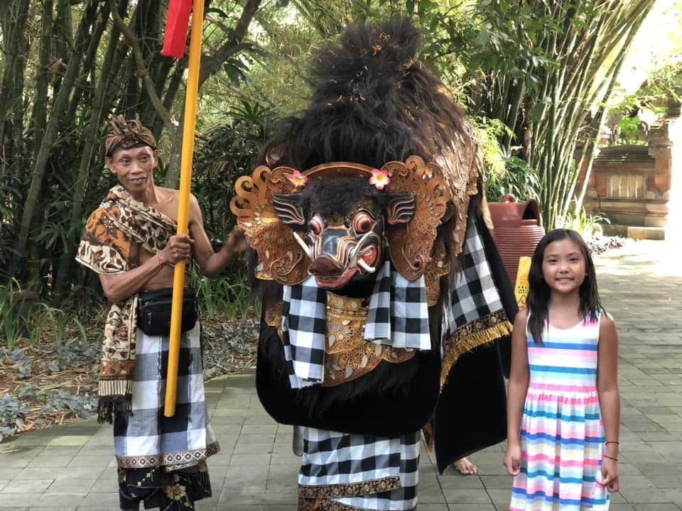 A young girl stands with a man and a Balinese elephant structure.