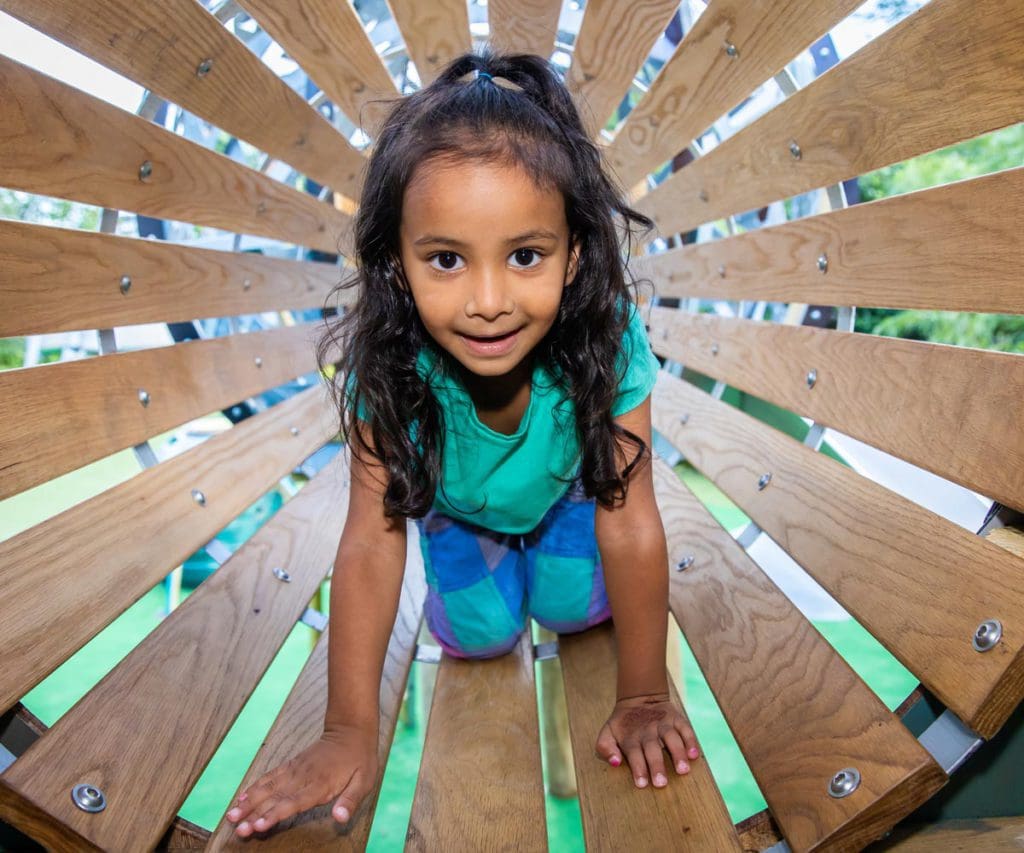 A young girl crawls through a wooden tunnel at the Discover Children's Story Centre, one of the best museums in London for kids.