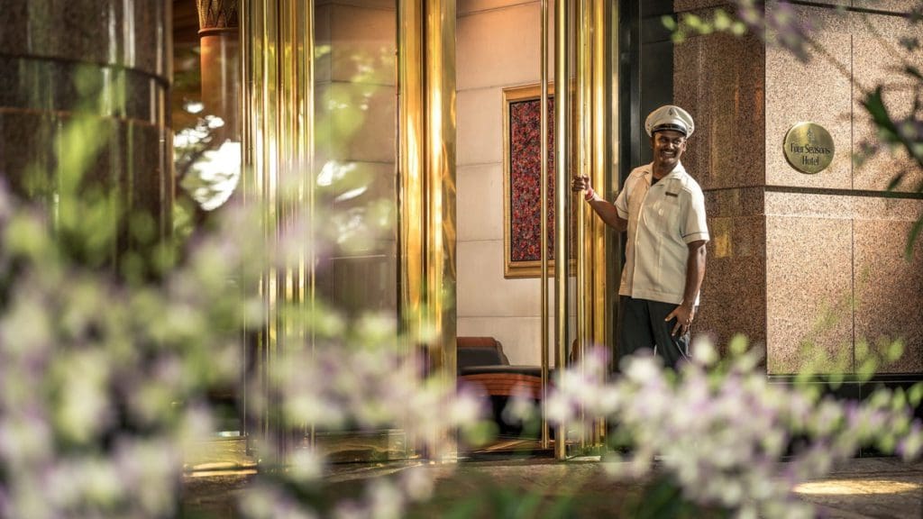 A staff member opens the entrance to Four Seasons Hotel Singapore, welcoming new guests.