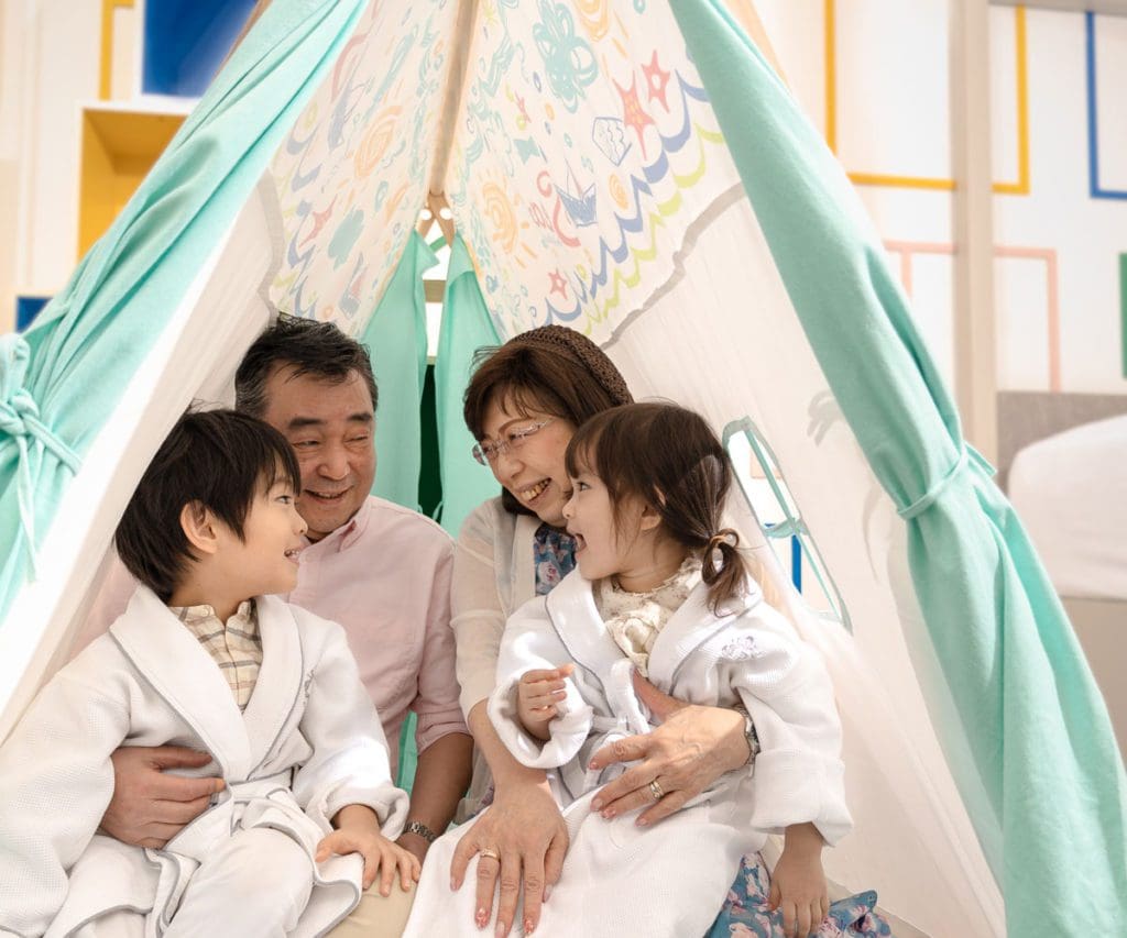 Two kids and their grandparents playing in an in-room tent for kids at Grand Park City Hall.