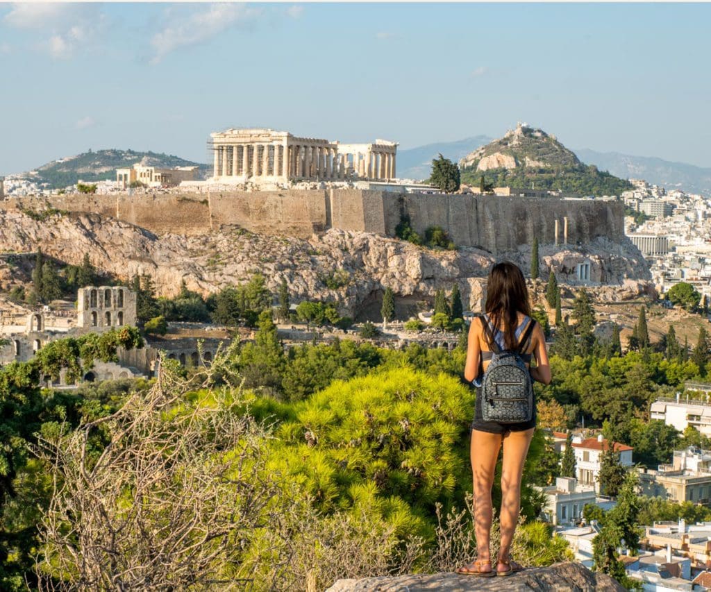 A teen girl stands on a hill looking across Athens to the acropolis. 