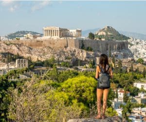 A teen girl stands on a hill looking across Athens to the acropolis.