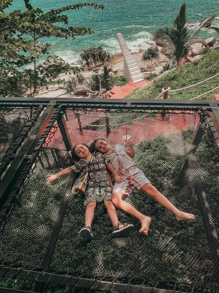 Two kids lay on a mesh canopy above a beach scene in Bali, one of the best places to visit in Asia with kids.