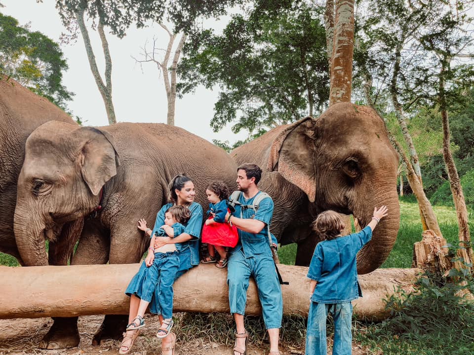 A family of five sits together with elephants behind them at Anantara Golden Triangle Elephant Camp & Resort in Thailand, one of the best places to visit in Asia with kids.