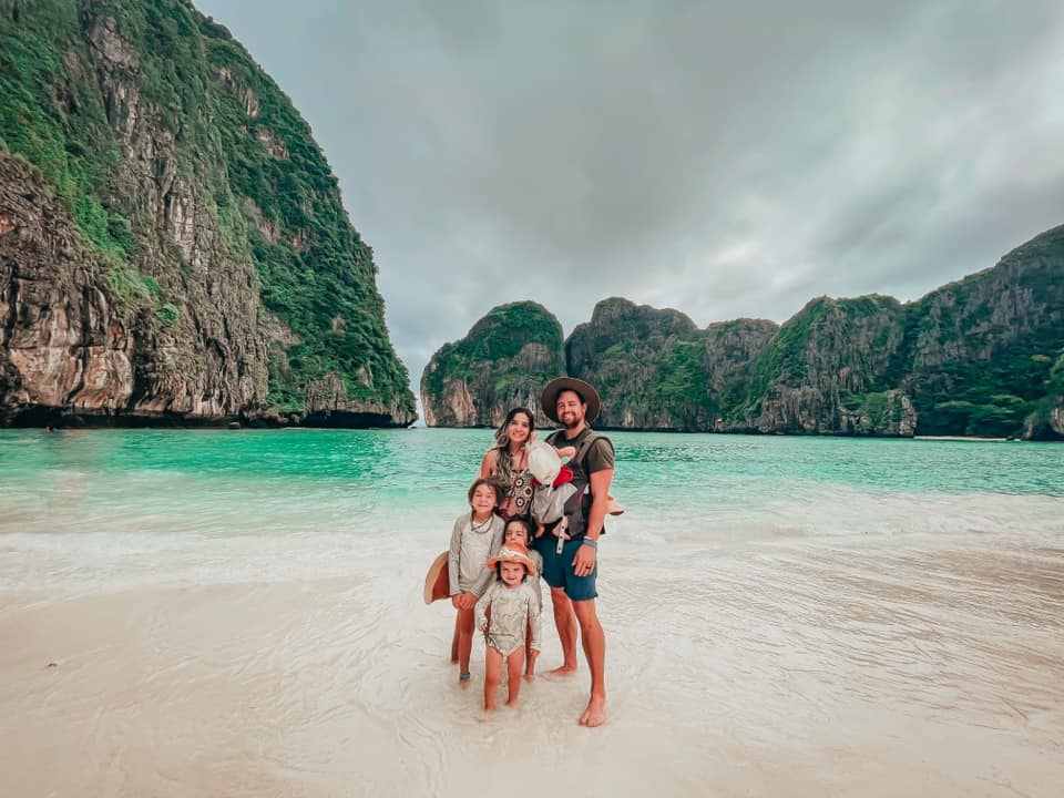 A family of five stands together on a beach on Phi Phi Island in Thailand.