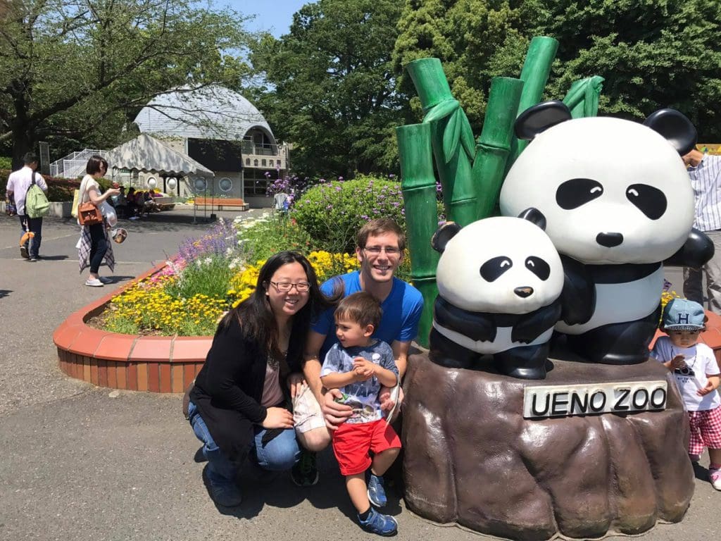 A family of three poses together at the entrance to Ueno Zoo.