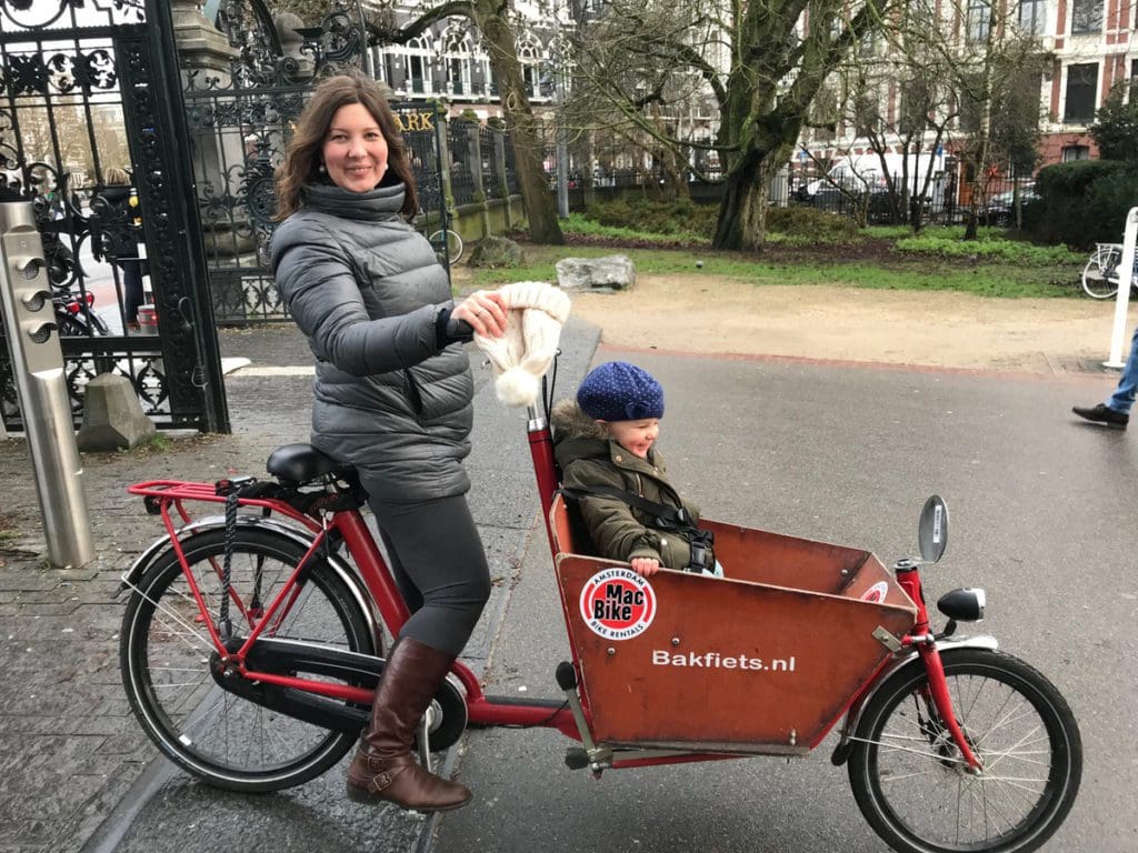 A mom sits on a bike, with a basket in front for her children in Amsterdam.