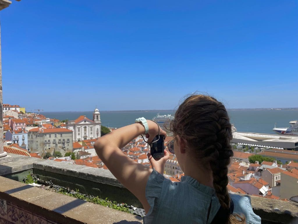 A young girl takes a picture from a view at Sao Jorge Castle, with Largo Santa Luiza in the distance, a fun stop on any Lisbon itinerary with kids.