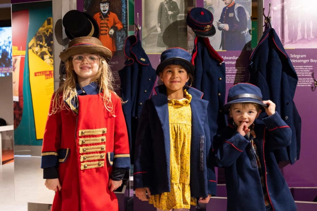 Three young kids dress up at an exhibition at The Postal Museum.