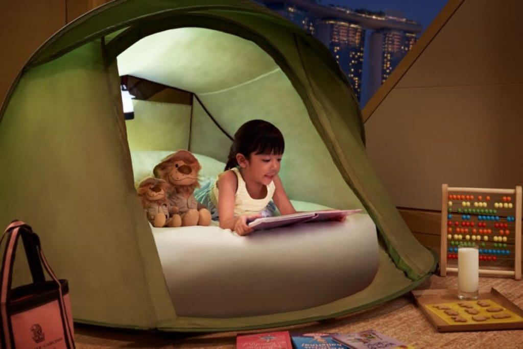 A young girl reads in a tent with her stuffies at The Ritz-Carlton, Millenia Singapore, one of the best hotels in Singapore with kids.