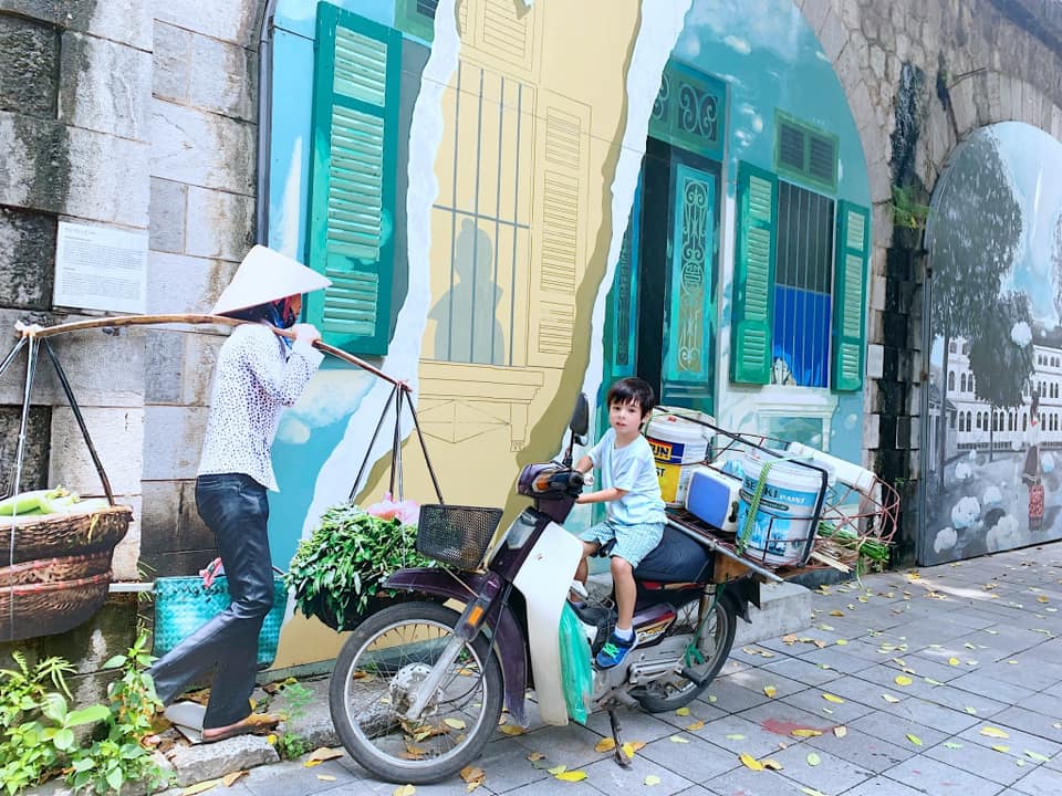 A young boy sits on a motorcycle in front of a mural in Hanoi.