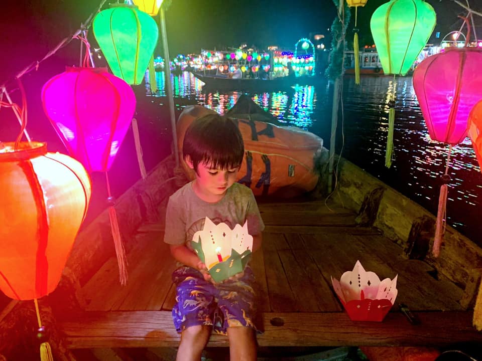 A young boy sits with a lantern boat during a festival in Hội An.