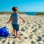 A young boy drags a sand bucket across the sand at Cape Cod.