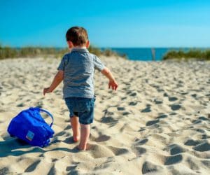 A young boy drags a sand bucket across the sand at Cape Cod.