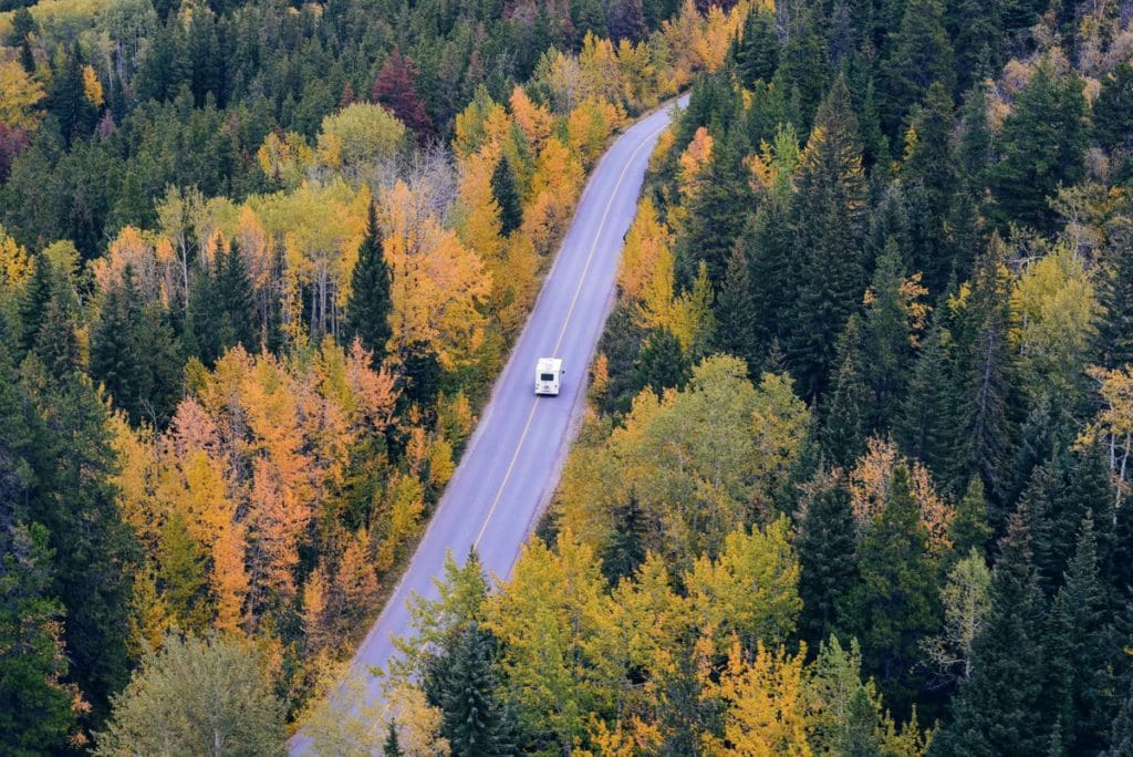 A drone shot of an RV traveling down an empty road, with a forest on each side.