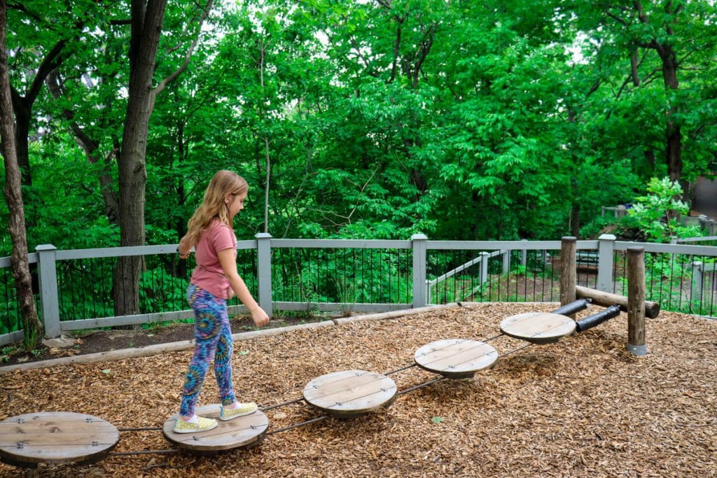 A young girl walks along a wooded path in the adventure park area of the Quebec City Aquarium, a must do on any Quebec City itinerary with kids.