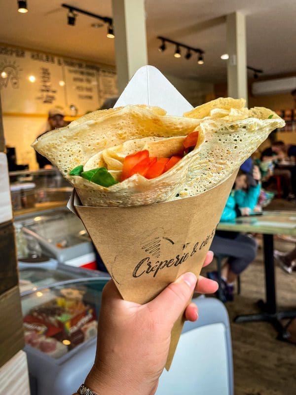 A hand holds out a savory crepe featuring tomatoes and greens, a must eat on any Quebec City itinerary with kids.