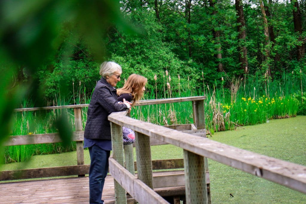 A young girl and her grandmother stand on a wooden platform look at a pond at Domaine de Maizerets.