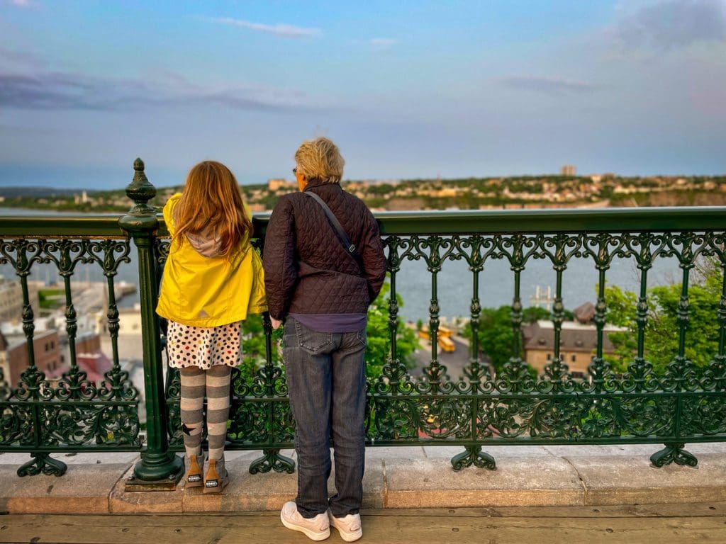 A young girl and her grandmother look over the railing onto a view of the Saint Lawrence River in Quebec City, a must see on any Quebec City itinerary with kids.