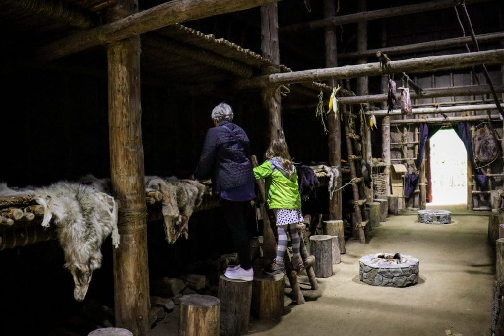 A young girl and her grandmother look at the displays inside the replica Long House at the Musée Huron-Wendat, a must do on any Quebec City itinerary with kids.