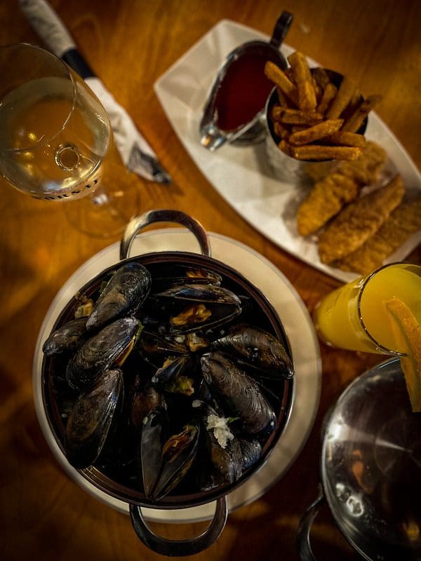 An table spread of mussels, wine, and kids' chicken strips at D'Orsay Pub in Old Quebec, a must eat on any Quebec City itinerary with kids.