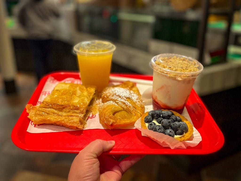 A stretched out hand holds a red tray of croissants and coffee at Paillard, a must eat on any Quebec City itinerary with kids.