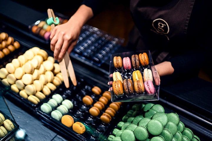 A hand reaches out and organizes colorful macarons on a plate.