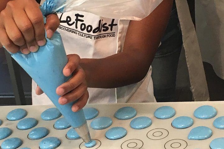 A hand pipes blue macarons on a Paris Cooking Class: Learn How to Make Macarons.