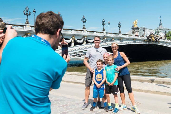 A man takes a picture of a family, while on the Paris Highlights Bike Tour with Eiffel Tower, Louvre, and Notre Dame.