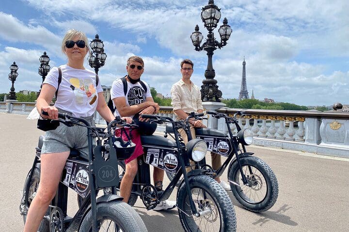 A family of three sits atop their respective electric bikes on a Paris street, while on a Paris Sightseeing Family-Friendly Guided Electric Bike Tour.