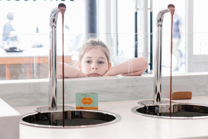 A young girl watches chocolate drip from a machine, while on the Pastry & Chocolate Family Tour in the Marais.