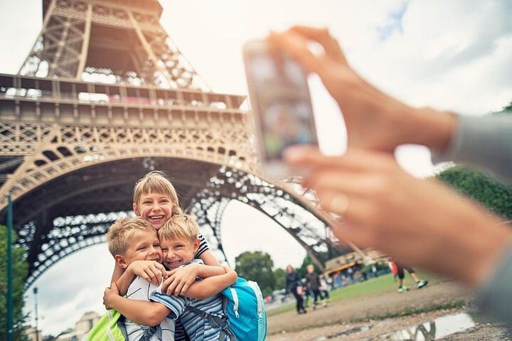 A mom takes a picture of her kids in front of the base of the Eiffel Tower, while on the Private Eiffel Tower Elevator Tour with Summit.