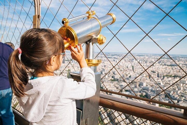 A young girl looks through a spy glass atop the Eiffel Tower, while on the Private Eiffel Tower Elevator Tour with Summit.