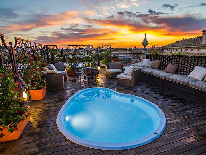 An outdoor terrace with a pool at Colonna Palace Hotel, with a sunset in the distance.