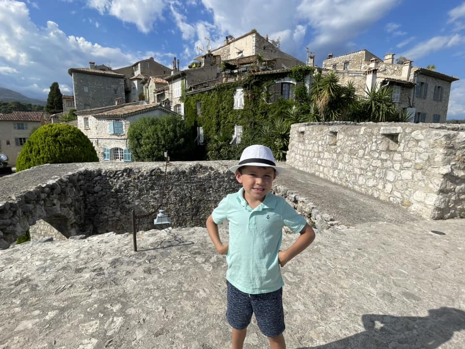A young boy stands outside of historic buildings, while exploring St. Paul de Vence, one of the best places to visit in France with kids.