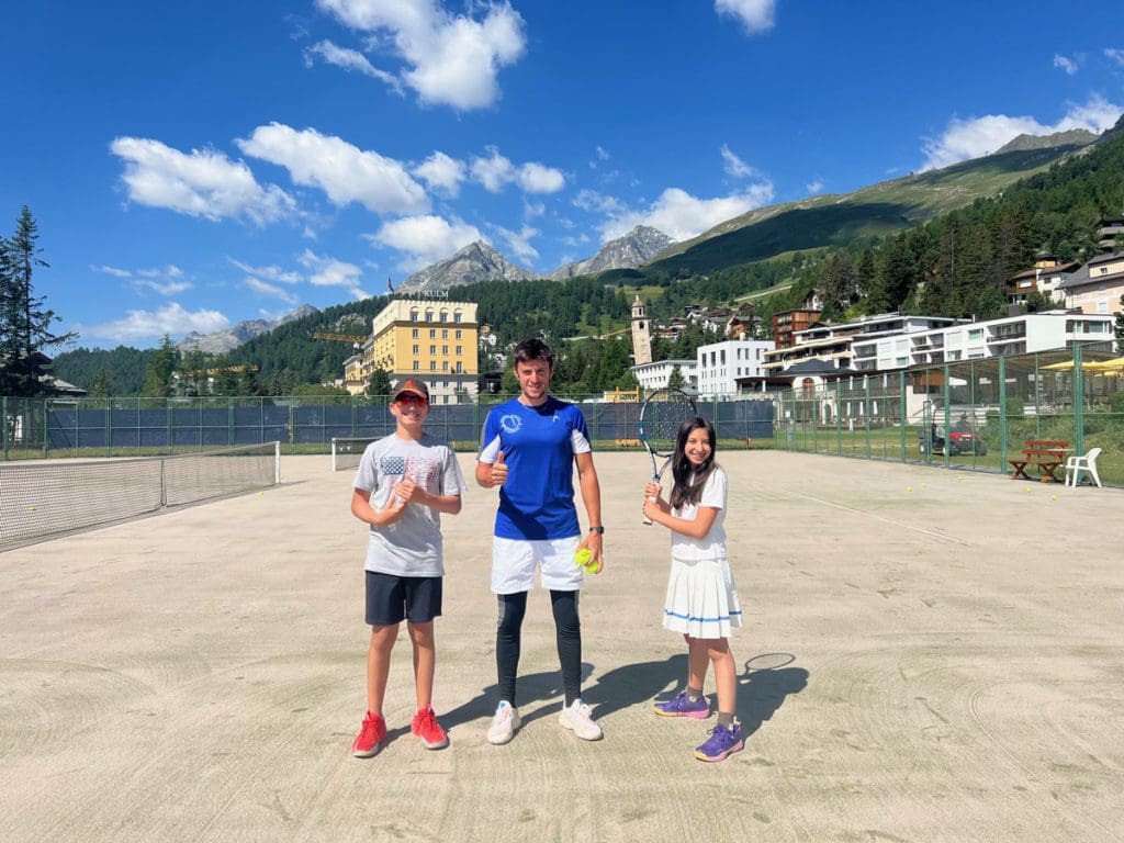 Two kids stand with a tennis instructor, while staying at Kulm Hotel, one of the things you'll learn about in this review of Kulm Hotel St. Moritz.