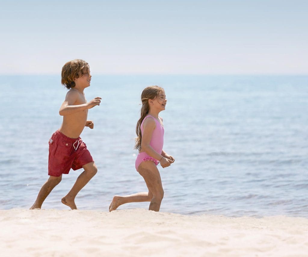 Two kids run across a Greek beach while staying at an Ikos Resort.